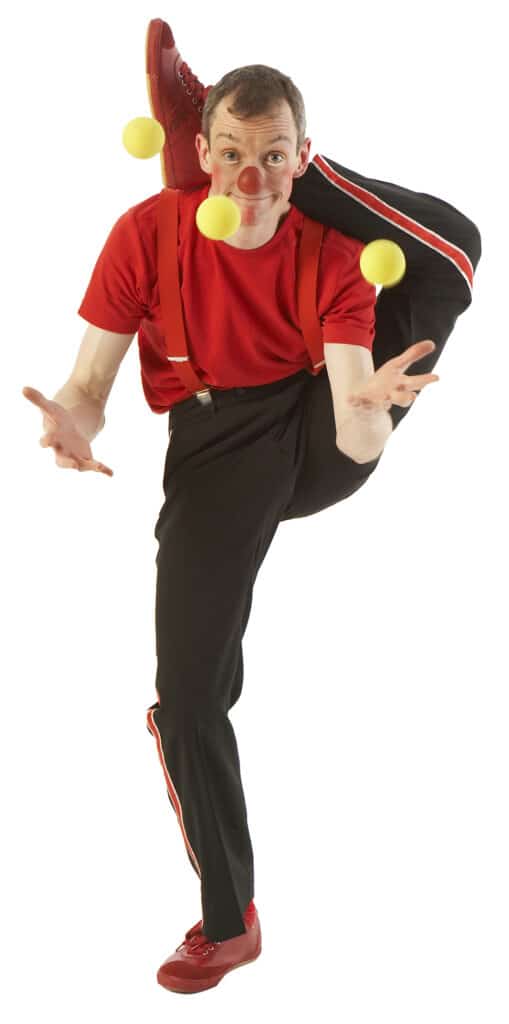 Klovnen Tapé jonglerer med det ene ben bag nakken